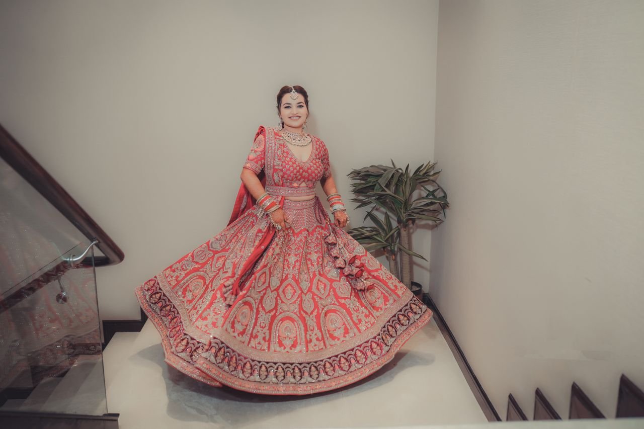 Smiling bride in ornate red lehenga posingin haya designer on her wedding day.